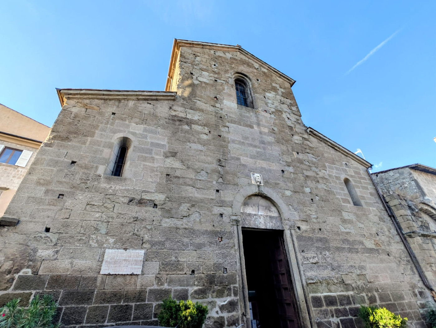 La sobria facciata romanica a capanna, in blocchi di peperino, con il portale principale sormontato da un bassorilievo classico